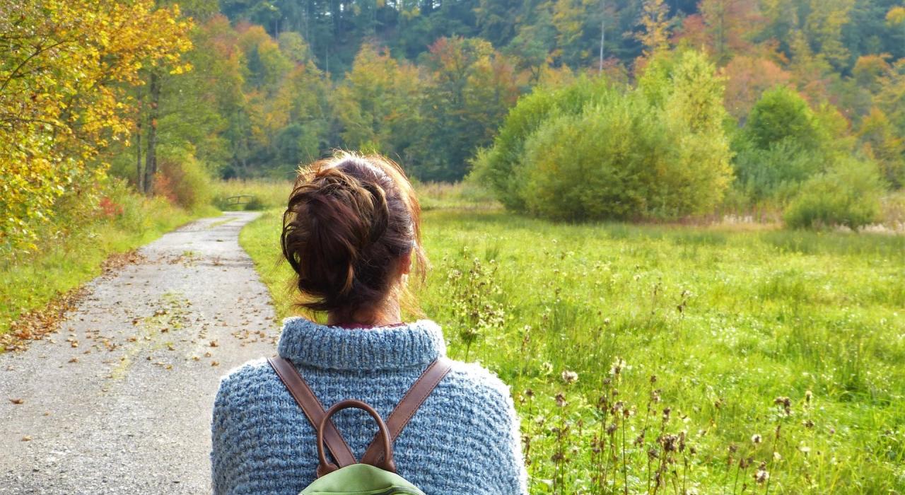 ba0fd254-166b-4da0-bb59-170f1903bcb1 Frau geht spazieren im Wald mit einem Rucksack und einem blauen Pulli
