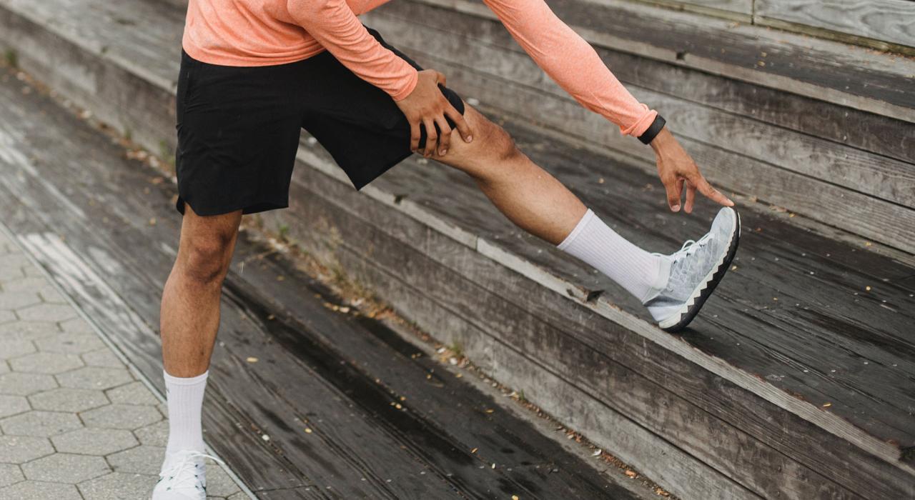 Eine Person in Sportkleidung, die ihre Beinmuskeln dehnt, indem sie ein Bein auf eine Holztreppe legt