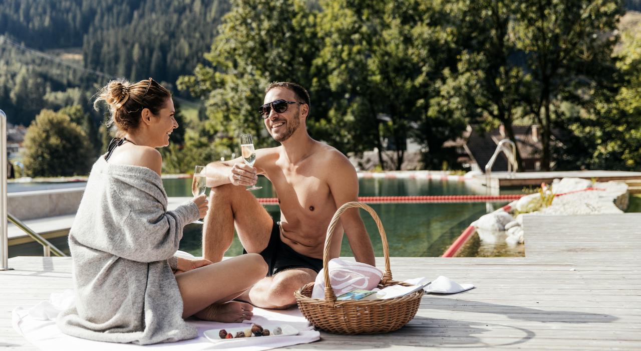 Ein Paar sitzt am Rand des Outdoor-Schwimmbads und stößt an