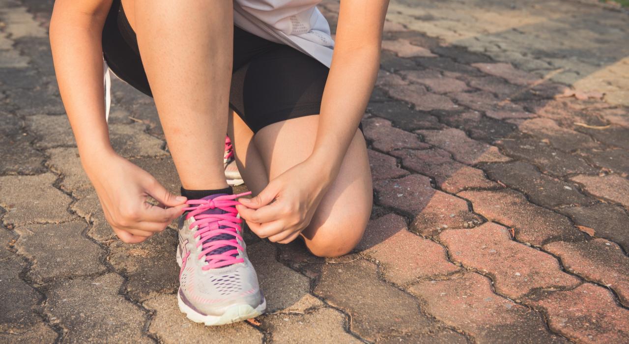 Eine Frau schnürt sich die Sportschuhe am Boden