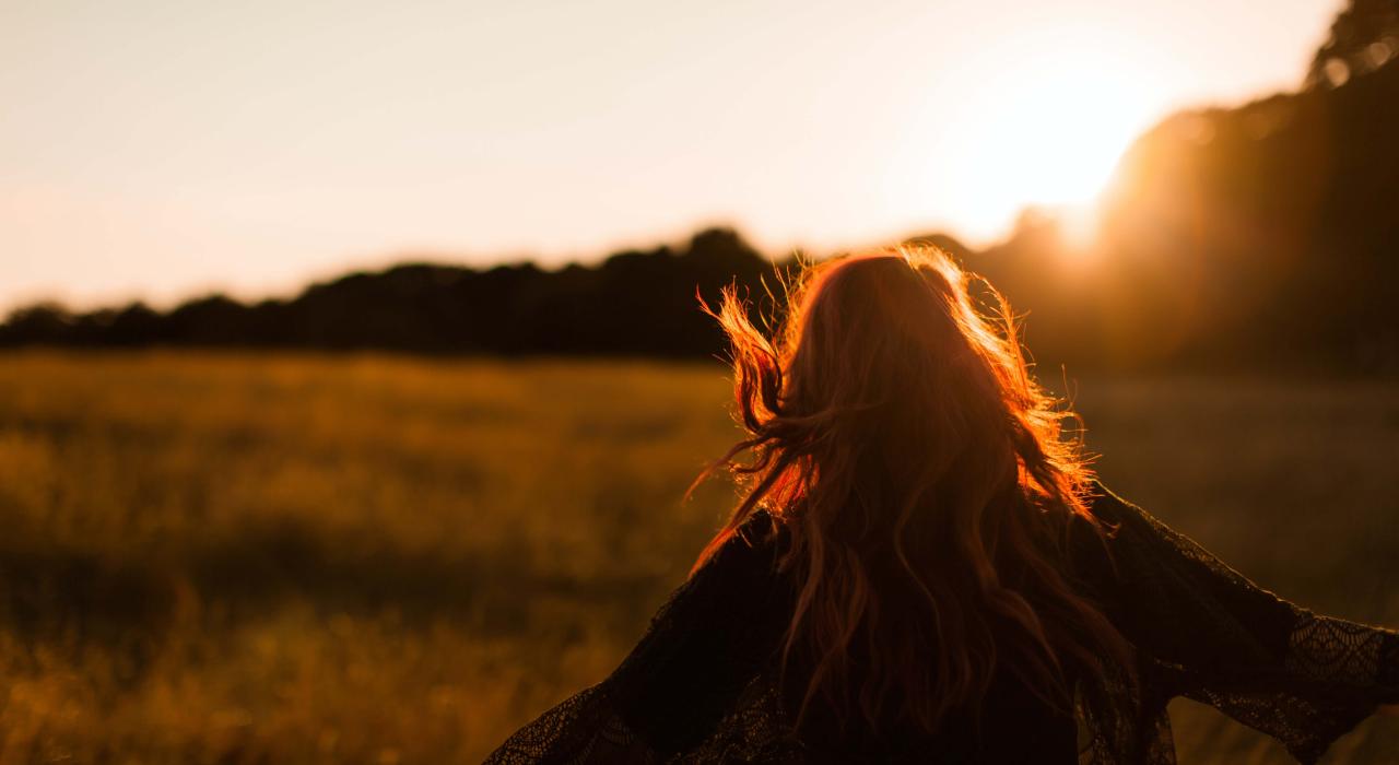 Frau steht mitten in einem Feld während die Sonne untergeht
