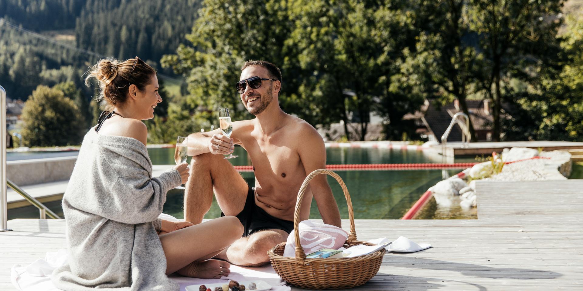 Ein Paar sitzt am Rand des Outdoor-Schwimmbads und stößt an