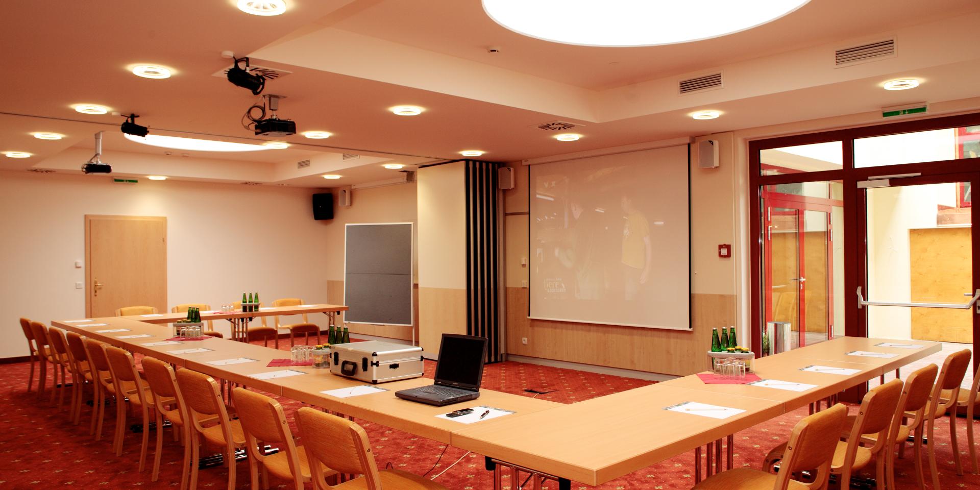 Blick in den Konferenzraum mit Konferenztisch und Stühlen in Richtung Projektor im Seminarhotel in Kärnten