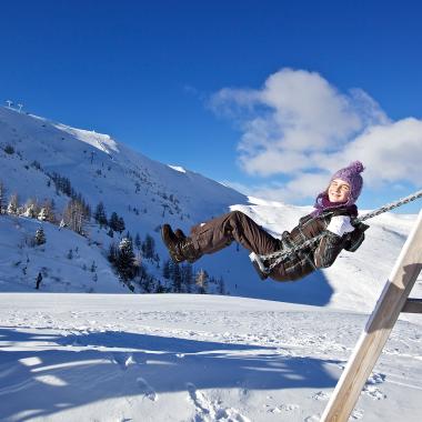 Ein Kind auf der Schaukel in den Bergen im Winter während des Urlaubs in unserem Familienhotel in Bad Kleinkirchheim