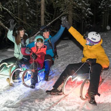 4 Menschen beim nächtlichen Schlittenfahren während ihres Winterurlaubs in unserem Familienhotel in Bad Kleinkirchheim