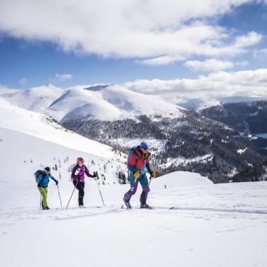 Drei Menschen beim Langlaufen in den Bergen während ihres Winterurlaubs in Kärnten