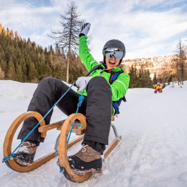 Eine Person schlittelt und lacht in die Kamera während ihres Winterurlaubs in Kärnten