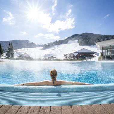 Eine Frau entspannt sich im Außenpool während ihres Winterurlaubs in Kärnten und genießt den Blick auf die schneebedeckten Berge