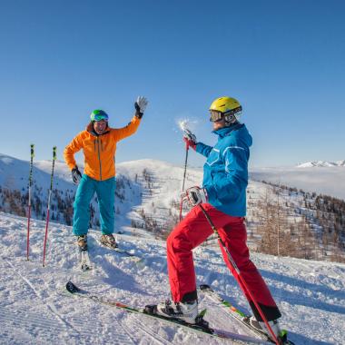 Ein Paar genießt einen sonnigen Tag beim Skifahren in Bad Kleinkirchheim. Mit farbenfroher Skibekleidung und perfekten Schneeverhältnissen erleben sie winterlichen Spaß pur.