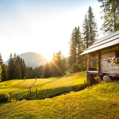 Ein Holzhaus bei Sonnenuntergang und in der Ferne Menschen beim Golfspielen im Sommerurlaub in Kärnten