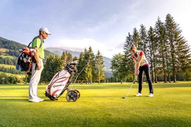 Ein Golfer beobachtet eine Frau, die sich auf einen Golfschlag vorbereitet, umgeben von Bergen