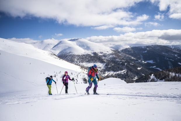 Drei Menschen beim Langlaufen in den Bergen während ihres Winterurlaubs in Kärnten