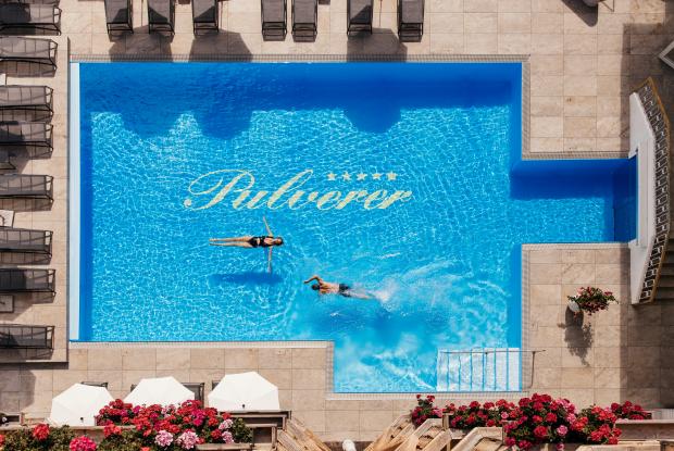 Ein Foto aus der Vogelperspektive von zwei Personen beim Schwimmen im Außenpool des 5 Sterne Hotels in Bad Kleinkirchheim.