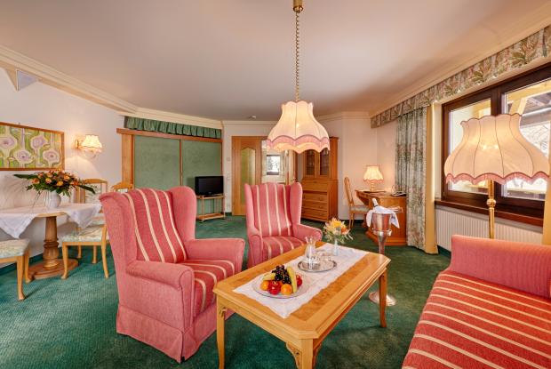 "Ein geräumiges Wohnzimmer in einem Hotelzimmer mit grünem Teppichboden, gestreiften Sesseln und Sofa