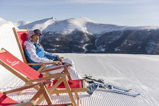 Eine Frau in ihrem Winterurlaub in Kärnten, die nach dem Skifahren auf einem Stuhl sitzt und die Sonne genießt