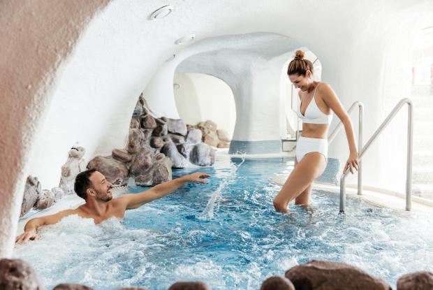Ein Mann im Whirlpool und eine Frau beim Betreten des Whirlpools im 5-Sterne-Hotel in Bad Kleinkirchheim