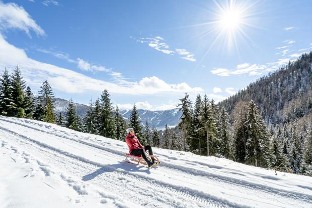 Eine Person, die im Winterurlaub in Kärnten bei Sonnenschein den Berg hinunterschlittelt