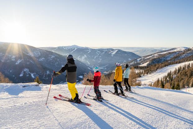 Drei Erwachsene und ein Kind beim Skifahren in den Bergen in ihrem Winterurlaub in Kärnten