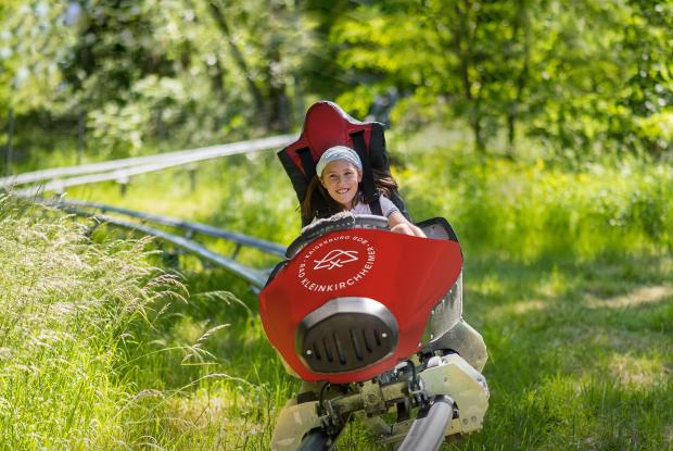 Ein kleines Mädchen genießt die Fahrt mit der Achterbahn in der Natur im Sommerurlaub in Kärnten