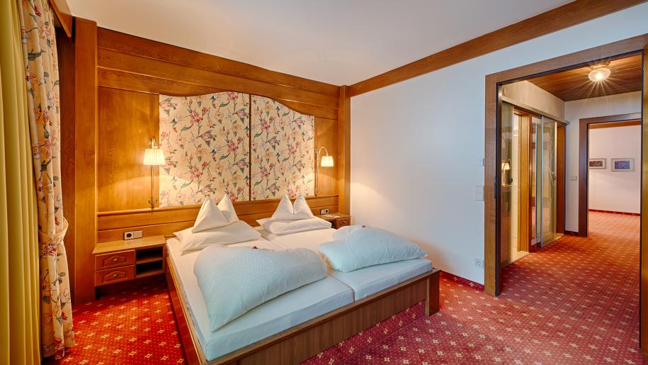 Ein gemütliches Hotelzimmer mit Doppelbett, Holzverkleidung, floralen Vorhängen und Teppichboden